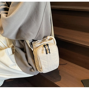 Sac bandoulière beige en nylon sur mannequin, avec cordon de serrage et doubles zips