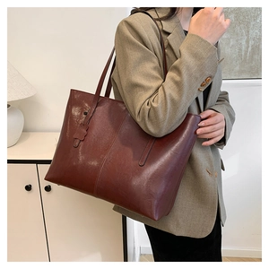 Macro detail of dark brown tote bag showing smooth PU leather texture and flower charm
