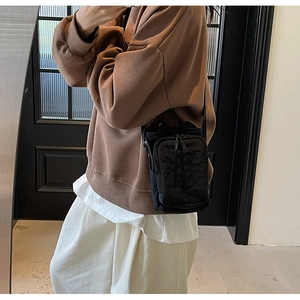 Détail d'un sac bandoulière en nylon noir porté avec un sweat brun et jupe beige