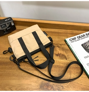 Top view of khaki nylon shoulder bag with black straps on a wooden table with props