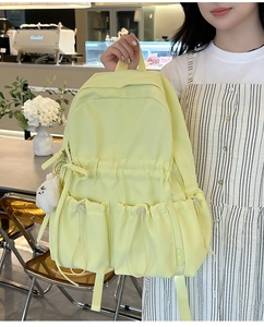 Detail of light yellow backpack with drawstring pockets and plush charm in a cafe setting