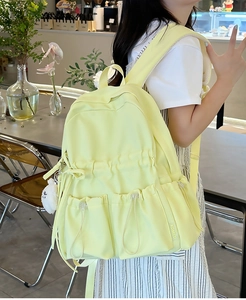 Detail of light yellow backpack with drawstring pockets and plush doll charm in cafe setting