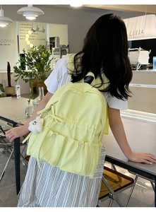 Detail of light yellow backpack with multiple pockets, drawstring and plush bear charm