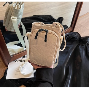 Détail du sac bandoulière en nylon beige avec fermeture à cordon et poche zippée à l'avant