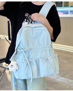 Detail of light blue nylon backpack featuring a drawstring closure and a plush bear charm