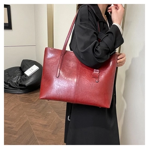 Large red tote bag with glossy leather texture and long handles shown on model's shoulder