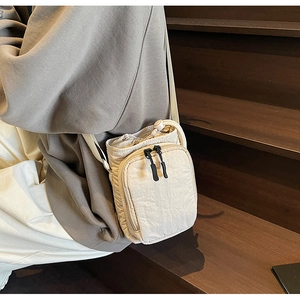 Détail du sac de téléphone en nylon blanc cassé avec cordon et poche zippée avant