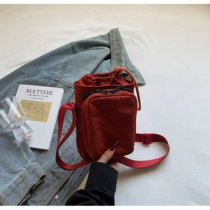 Détail du sac à bandoulière en nylon rouge brique avec cordon et poche zippée à l'avant