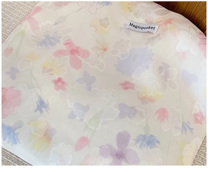 Dettaglio del tessuto jacquard con motivi floreali pastello ed etichetta logo