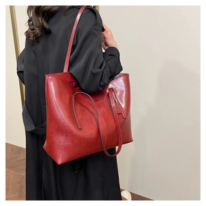 Detail of red leather tote bag with glossy finish and long shoulder straps worn on coat