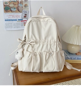 Close-up of cream school backpack featuring a decorative bow and plush pendant details