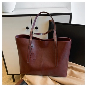 Close-up of deep red leather tote bag with vertical stitching and bear pendant