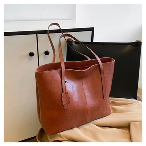 Close-up of brown leather tote bag with vertical stitching and wavy edge bag charm