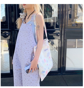 Dettaglio di borsa tote in tela tie-dye con etichetta e abito floreale viola