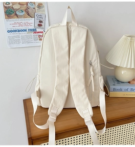 Detail of cream school backpack featuring hidden anti-theft back pocket and side bottle pouch