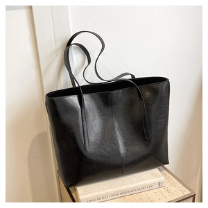 Detailed view of black faux leather tote bag with vertical stitching and glossy oil wax finish