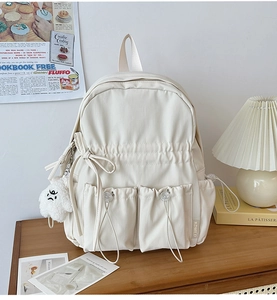 Detail of cream backpack showing dual drawstring front pockets and cute plush charm