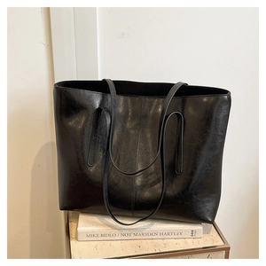 Detail of the high-shine black leather tote bag with minimalist stitching on a stone surface