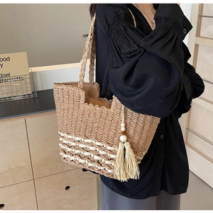 Detalle del bolso tote de paja tejida con bandas decorativas blancas y borla de cuentas