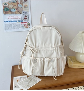 Detail view of cream backpack featuring drawstrings, cute bowknot, and side buckle
