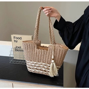 Detalle de un bolso tote de paja tejida con borlas de color crema y cuentas de madera
