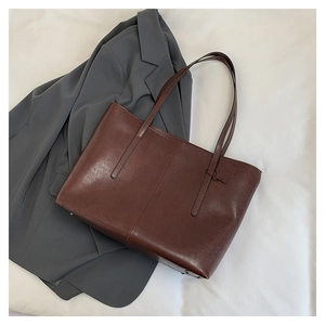 Close-up of vintage dark brown faux leather tote bag with butterfly charm on white fabric