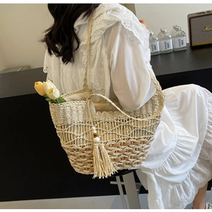 Detalle de bolso de paja tejida con toques marrones, borlas de color beige y forro