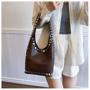 Detail einer braunen Ledertasche mit Vintage-Silbernieten auf der Schulter des Models