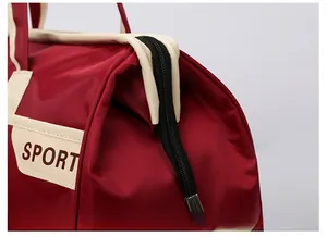 Detail of a red travel duffel bag showing a black zipper closure and SPORT logo patch