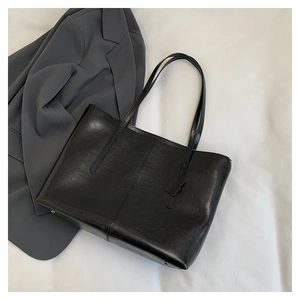 Detail view of large black tote bag with petal charm accessory on a classic grey suit