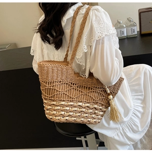 Detalle del bolso tote de paja con diseño de ondas caladas y un colgante de borla