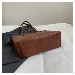 Detail showing the bottom metal rivets and texture of the brown faux leather tote bag
