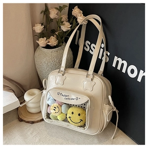 Detail view of cream shoulder bag featuring transparent pocket with plush smiley charms