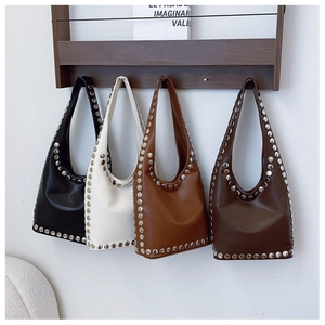 Detailansicht von vier Nietenschultertaschen in Schwarz, Beige und Braun an einem Holzregal