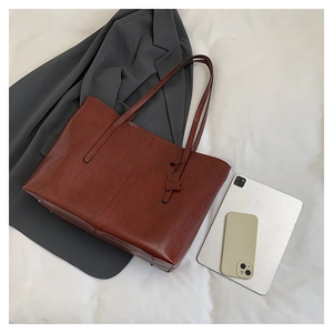 Brown vintage leather tote bag shown with daily essentials on a white fabric surface