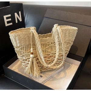 Detalle del bolso tote bohemio de paja tejida con borlas decorativas y detalles de cuentas