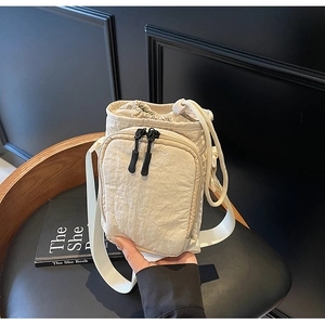 Gros plan du sac bandoulière crème avec cordon de serrage et poche zippée avant