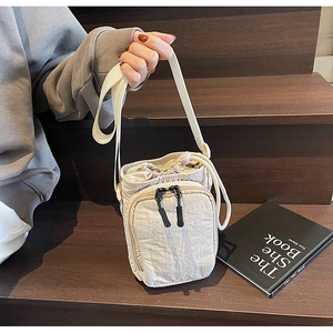 Détail du sac bandoulière en nylon beige avec cordon de serrage posé sur un escalier en bois