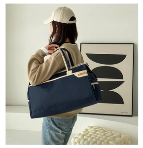 Large blue travel bag with white straps shown on shoulder in minimalist interior