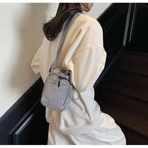 Détail d'un sac bandoulière en nylon gris imperméable avec cordon porté par un mannequin