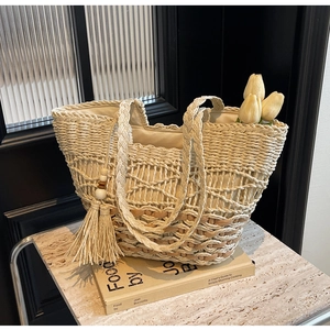 Detalle de bolso tote de paja tejida beige con patrones calados y borlas decorativas