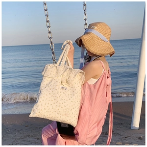 Chic cream floral tote bag in pleated fabric shown in a scenic beach setting