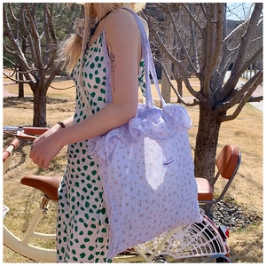 Outdoor shot of light purple floral tote bag with ruffled edges and vintage bicycle detail