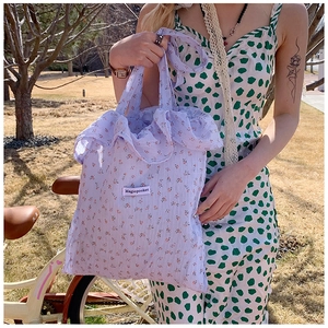 Detail of lavender floral tote bag with ruffle trim and logo in a garden setting