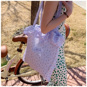 Close-up of a floral canvas tote bag in light purple with red flower patterns in a garden