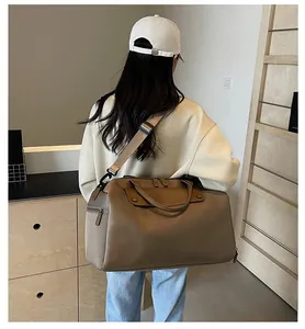 Rear view of a model carrying a large brown Oxford travel bag in a minimalist room
