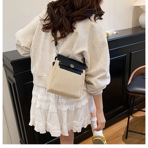 Detail of a beige woven crossbody bag with black leather trim worn in a lifestyle setting