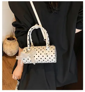 Close-up of white cylindrical Boston bag with black polka dots and lace bow detail