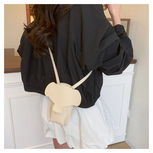 Detail shot of a creative elephant-shaped crossbody bag in cream leather worn by a model
