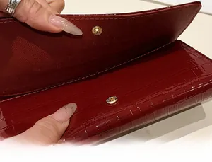 Détail d'un sac à main rouge foncé brillant à motif crocodile avec fermoir doré en métal